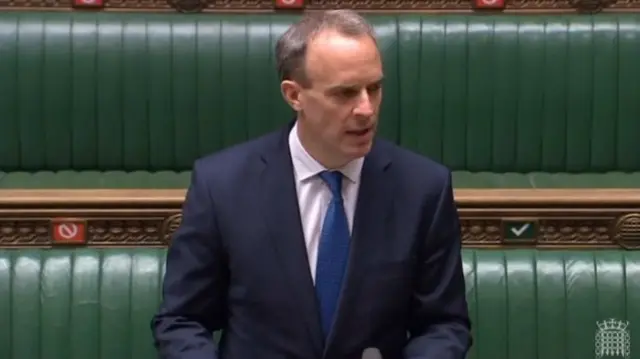 Dominic Raab, a man wearing a dark suit and blue tie, speaking in the House of Commons, with empty green benches behind him