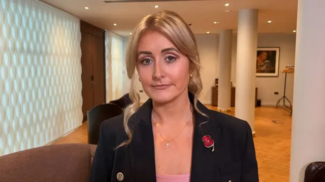 Katie Amess wears a black jacket and has blonde hair in a ponytail