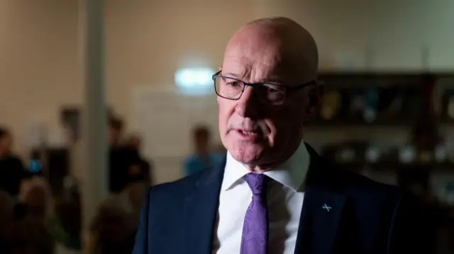 John Swinney wears a blue suit and purple tie