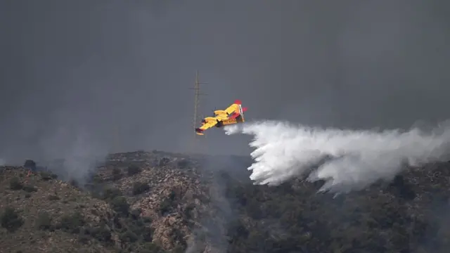 A plan drops a liquid substance on a dry hillside in Spain