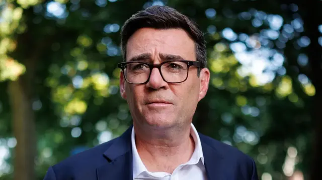 Andy Burnham, a man wearing a navy blazer, white shirt and glasses.