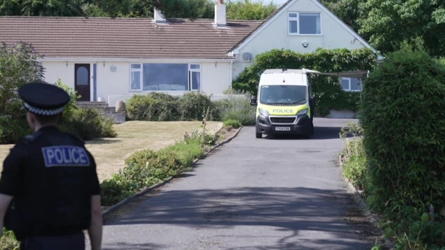 A view of a house with a police van parked outside it and a police officer walking up the drive