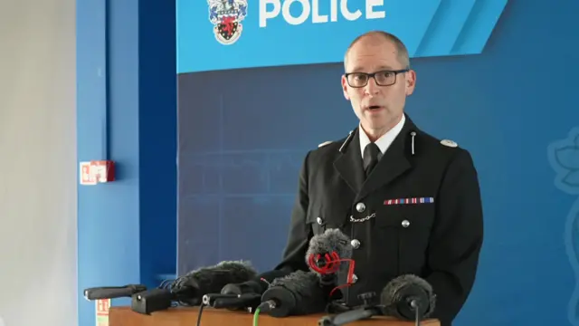 Headshot of Longman who speaks into microphones propped up on a stand