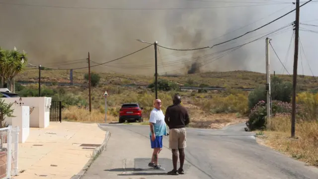 Residents talk as they get ready to leave their homes while smoke and flames rise during a wildfire in Los Gallardos, Almeria, Spain, July 10,
