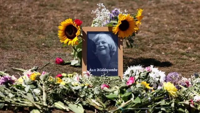 Flower tributes lie next to a portrait of Ann Widdecombe after she was found dead