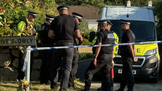 Police men and a car outside a home, a police cordon is in place.