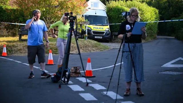 Media staffers are positioned in front of a police cordon at the entry road to Widdecombe's property.