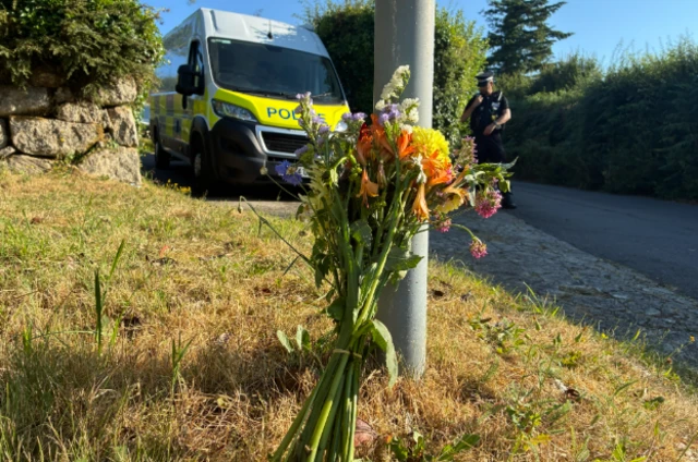 A bunch of flowers resting on a post, police in the background.