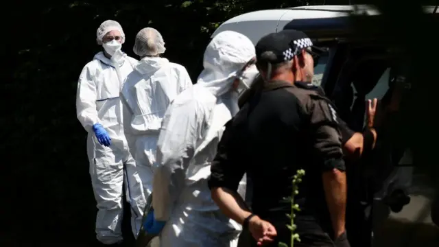 Three forensics officers are seen near Ann Widdecombe's home wearing white outfits with masks and gloves. Two police officers dressed in black are seen in the front of the picture