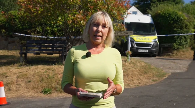 The BBC's Janine Jansen stands on the road outside Ann Widdecombe's home with a notepad and speaks to the camera