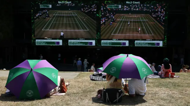 Spectators watch Wimbledon on big screens under umbrellas