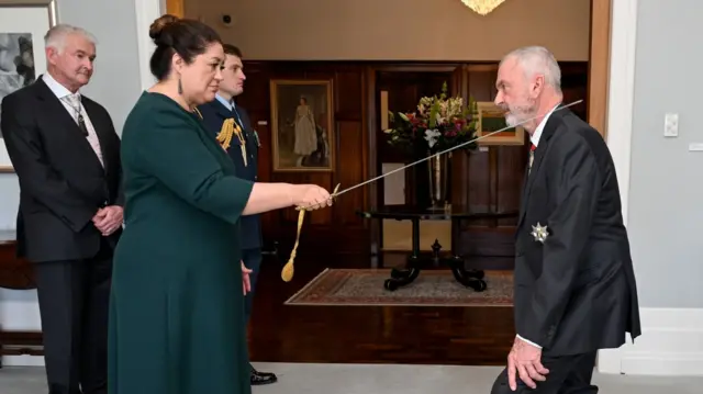 Sam Neill being knighted by Governor-General of New Zealand Dame Cindy Kiro with a sword in 2022