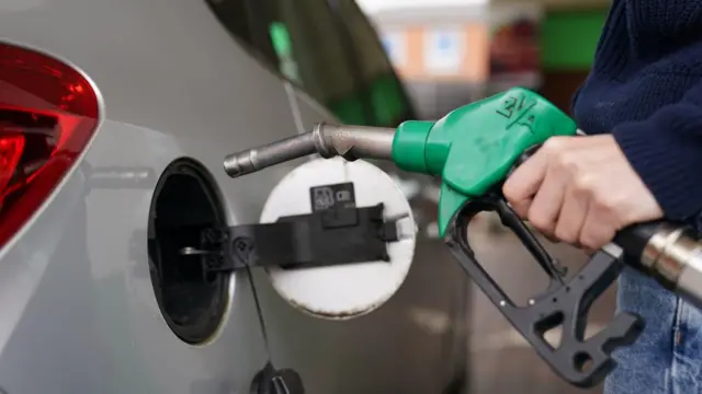 A man holding a petrol pump next to a car.