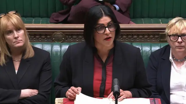 Mahmood speaking while holding a piece of paper in a folder