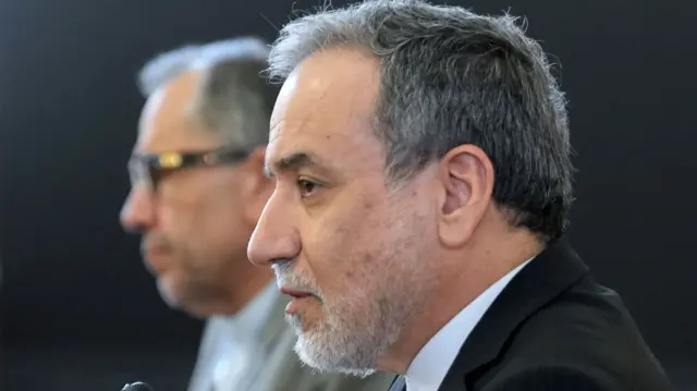 Abbas Aragchi picturd from the side speaking into a microphone and wearing a grey suit