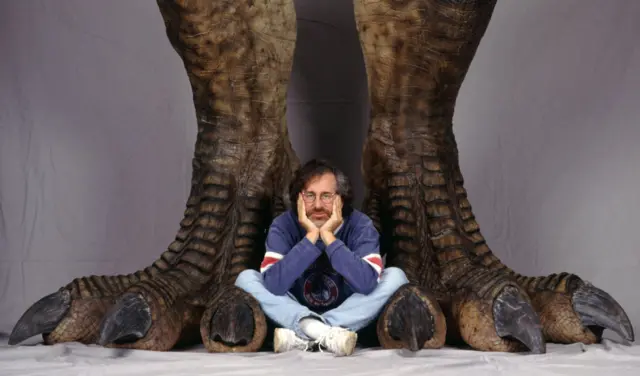 Director Steven Spielberg poses between a pair of giant dinosaur feet in a publicity still for the film 'Jurassic Park', 1993.