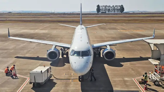 A plane is being refuelled on a runway during a sunny day