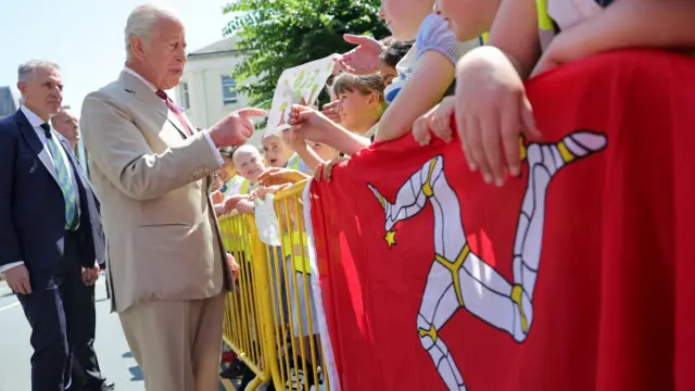 The King meets schoolchildren beside a large Isle of Man flag