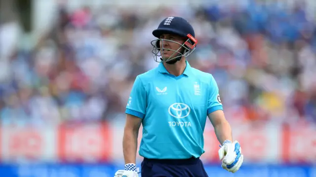 Harry Brook, wearing a bright  blue England shirt and dark blue helmet, looks annoyed as he walks off