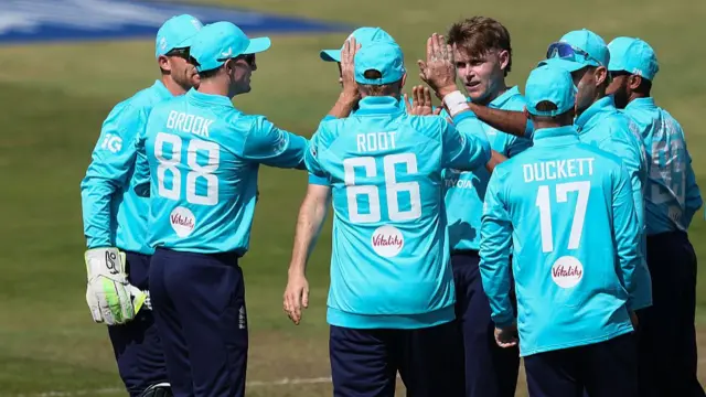 Sam Curran, surrounded by teammates wearing bright blue England shirts, celebrates his wicket
