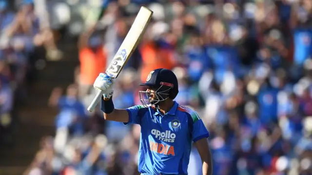 Axar Patel, wearing a blue India shirt and dark blue helmet, holds his bat aloft in his right hand