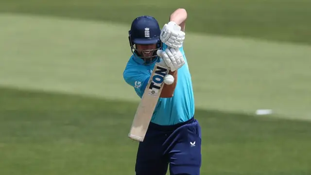 Will Jacks, wearing a bright blue shirt and dark trousers/helmet, plays defensively with his bat straight in front of his body