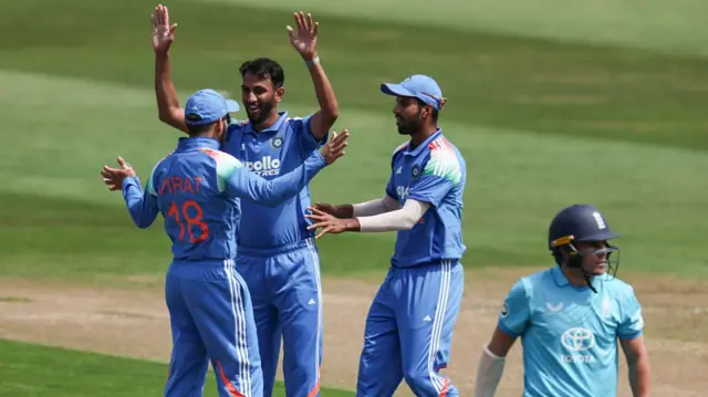 Prasidh Krishna (second left), wearing blue, holds his hands up to celebrate the wicket of Sam Curran (right), in pale blue), with two teammates celebrating in front of him