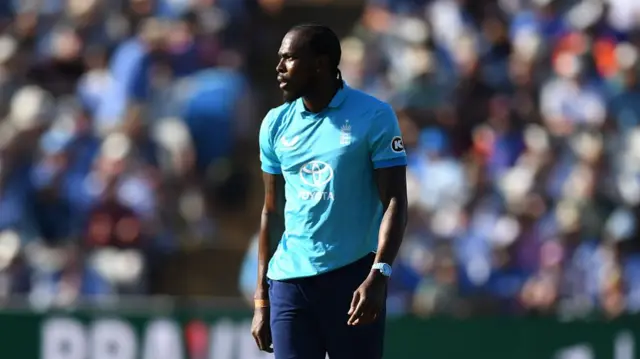 Jofra Archer, wearing a bright blue England shirt and dark blue trousers