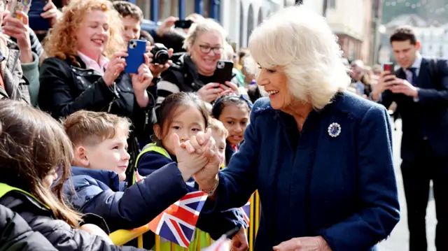 Queen Camilla in a blue coat shakes the hand of a schoolchild during her visit to the Isle of Man