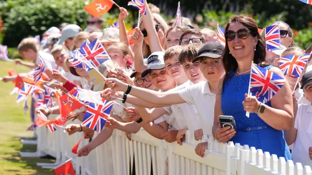 Children and a woman in a blue dress wave union jacks and Isle of Man flags
