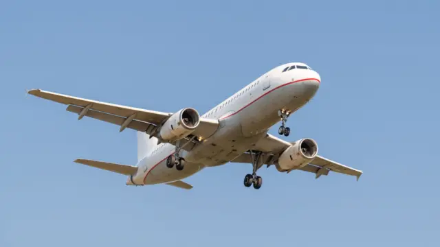 Commercial jet aircraft in flight against a blue sky, approaching for landing with its landing gear down