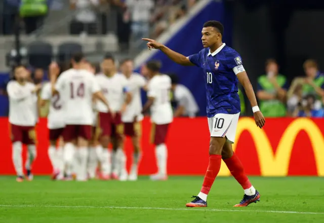Spain celebrate in the background as Mbappe gees up his teammates