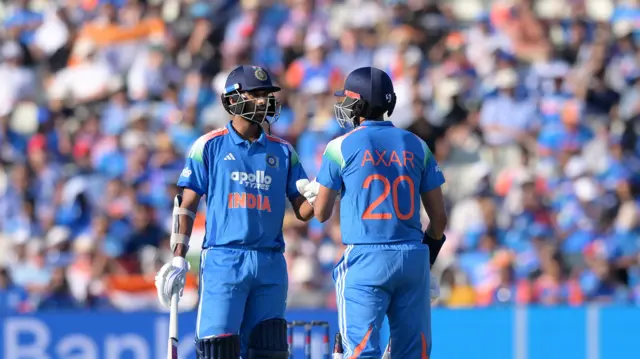Washington Sundar (left) and Axar Patel (right, facing away from the camera) touch gloves, with both wearing blue India kits and dark blue helmet