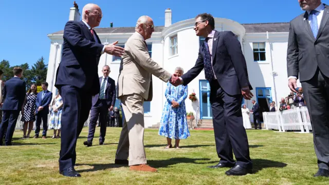 King Charles shakes hands with a man at a garden party