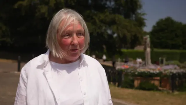 Lesley Clark has short grey/blonde hair and wears a white t-shirt and white jacket
