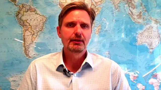 A man wearing a shirt, with a map of the world behind him.
