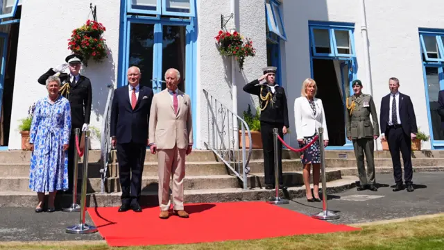 The King and dignitaries stand to attention for the national anthem outside Government House