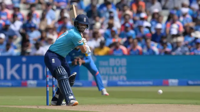 Ben Duckett, wearing a bright blue shirt and dark blue helmet and trousers, prepares to play a shot, with his bat held up to his left shoulder and the white ball bouncing towards him from the right