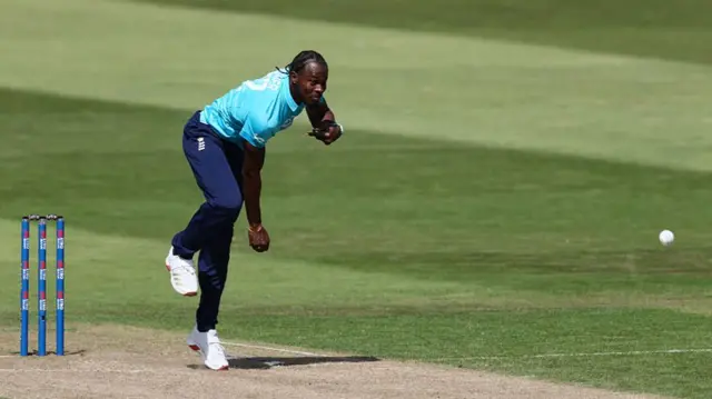 Jofra Archer, wearing a bright blue shirt and dark trousers, bowling