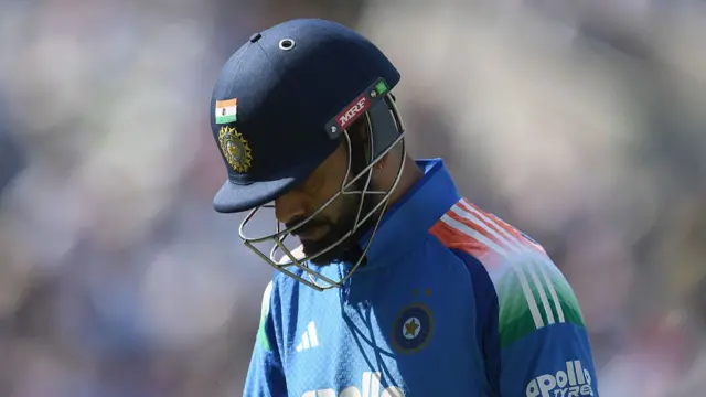 Head and shoulders of Virat Kohli, wearing a blue India shirt and dark blue helmet, walking off with his head down
