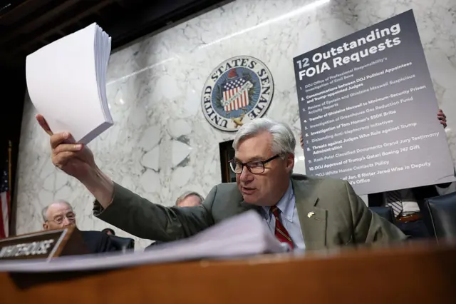 Sheldon Whitehouse holds a stack of white papers in the air