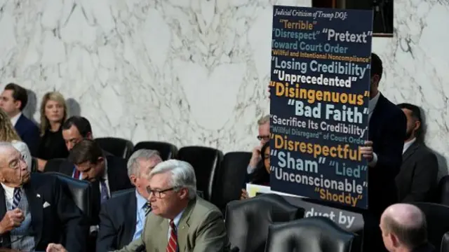 An aide of Sheldon Whitehouse holds a poster of "Judicial Criticism" of Trump's Department of Justice