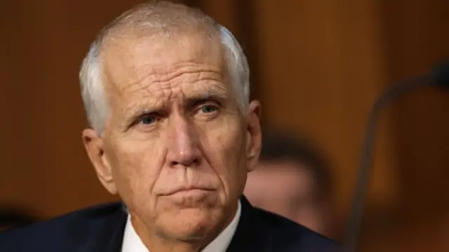 Thom Tillis wears a suit jacket, white shirt and yellow striped tie