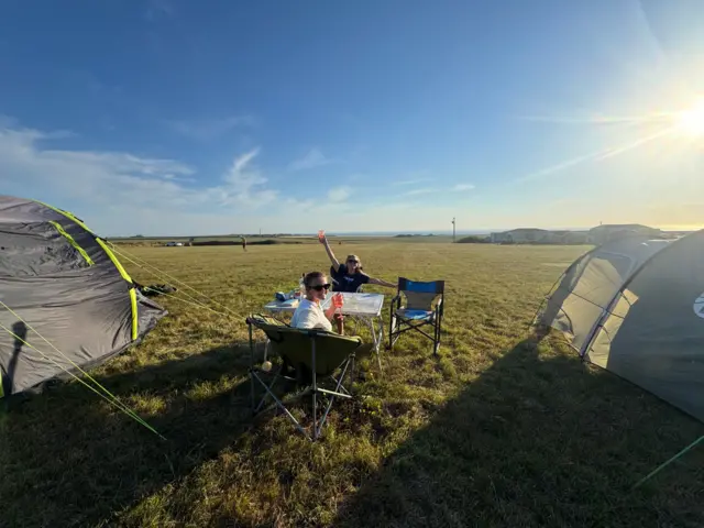 Two tents with two people sat at a table