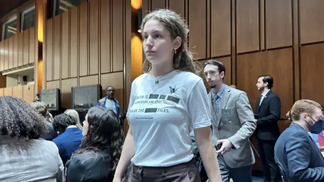 A woman wears a t-shirt that reads "Survivors are still waiting. Release the files" on it