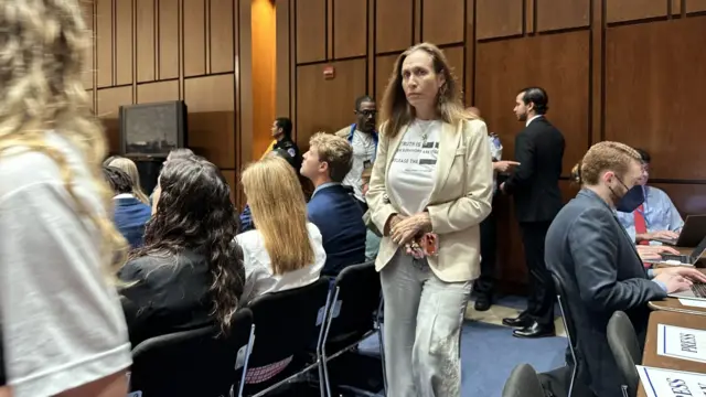 A woman wears a t-shirt that reads "Survivors are still waiting. Release the files" on it