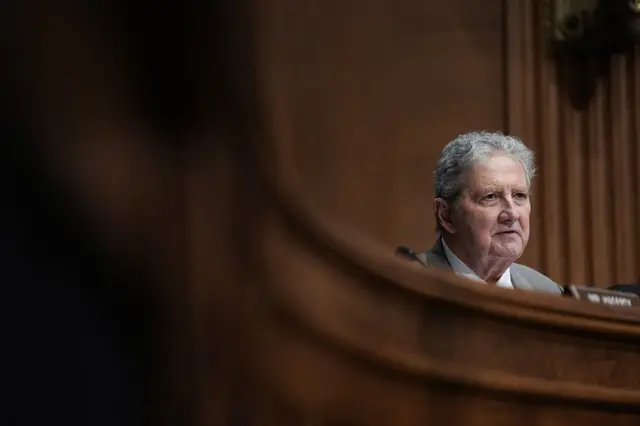 Senator Kennedy framed the dark wood dais and a dark wood wall