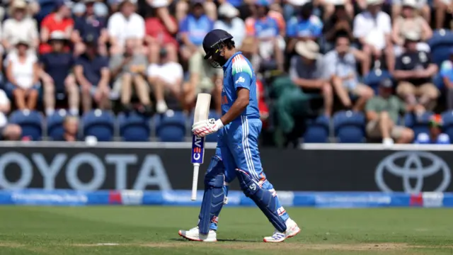 Rohit Sharma, wearing all blue and dark blue helmet, walks off with his head down and his bat in his left hand