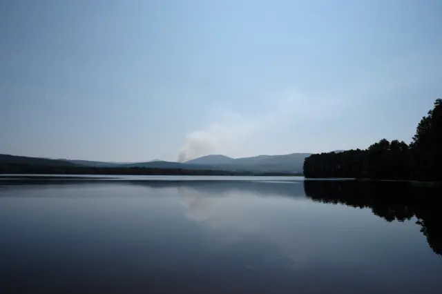 Viiew of loch looking over towards trees and smoke rising in the distance