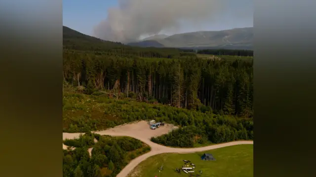 Campsite with just a few tents in a clearing beside a forest with smoke in the distance